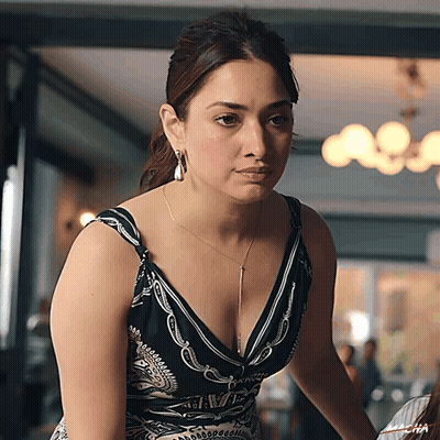 A Woman In A Black And White Dress With A Plunging Neckline Is Looking At The Camera GIF