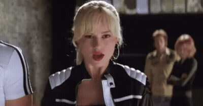 A Woman In A Black And White Jacket Is Standing In Front Of A Group Of People And Looking At The Camera . GIF