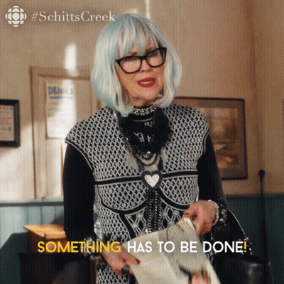 A Woman In A Black And White Outfit Is Holding A Newspaper And Says Something Has To Be Done GIF