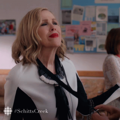 A Woman In A Black And White Outfit With Red Lipstick And A #Schittscreek Logo GIF