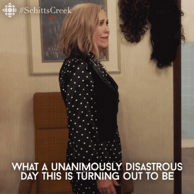A Woman In A Black And White Polka Dot Dress Is Standing In Front Of A Wall With Wigs On It GIF