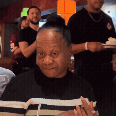 A Woman In A Black And White Striped Shirt Is Smiling In A Restaurant GIF