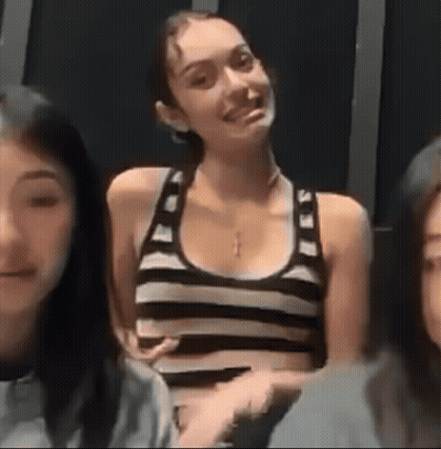 A Woman In A Black And White Striped Tank Top Is Smiling While Sitting Next To Two Other Women . GIF
