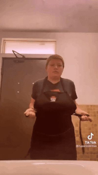 A Woman In A Black Apron Is Standing In Front Of A Sink In A Bathroom . GIF
