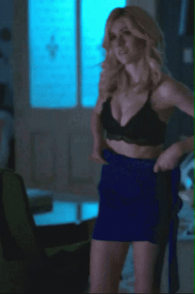 A Woman In A Black Bra And Blue Skirt Is Standing In A Living Room GIF