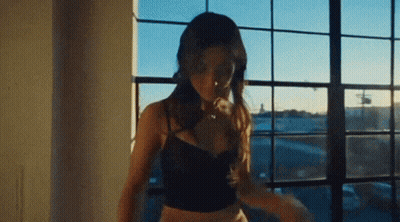 A Woman In A Black Bra Is Standing In Front Of A Window . GIF