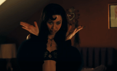 A Woman In A Black Bra With A Cross Necklace Is Standing With Her Arms Outstretched GIF