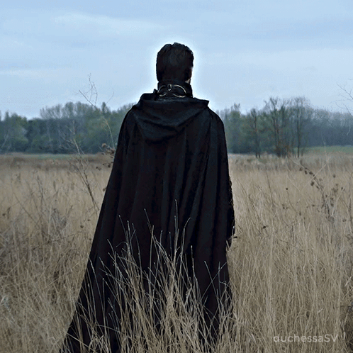 A Woman In A Black Cape Stands In A Field GIF