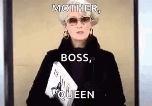 A Woman In A Black Coat And Sunglasses Is Holding A Magazine And A Laptop . GIF