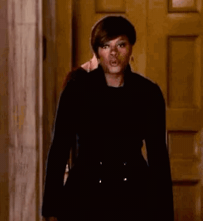 A Woman In A Black Coat Is Standing In Front Of A Door Making A Funny Face . GIF