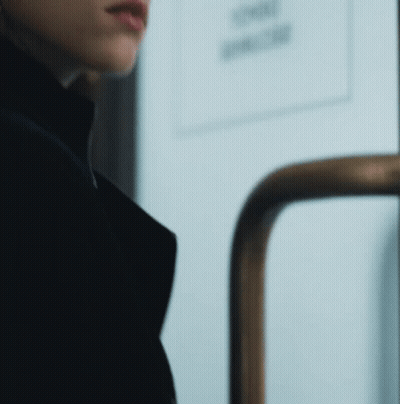 A Woman In A Black Coat Is Standing In Front Of A Door With A Sign That Says Smoking GIF