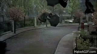 A Woman In A Black Coat Is Walking Down A Sidewalk . GIF