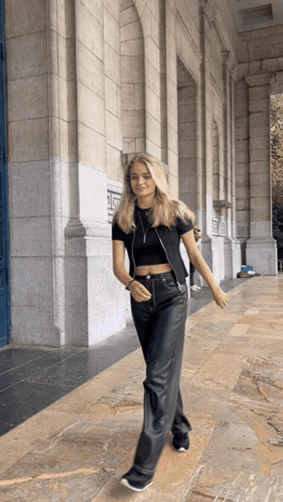 A Woman In A Black Crop Top And Black Leather Pants Walks In Front Of A Building GIF