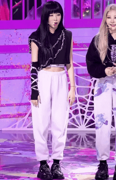 A Woman In A Black Crop Top And White Sweatpants Is Standing On A Stage With Another Woman . GIF