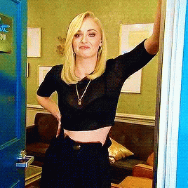 A Woman In A Black Crop Top Is Standing In Front Of A Blue Door In A Living Room . GIF