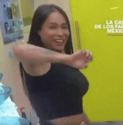 A Woman In A Black Crop Top Is Standing In Front Of A Yellow Door That Says La Venta De Los Famosos Mexico . GIF