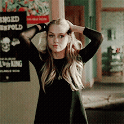 A Woman In A Black Dress Adjusts Her Hair In Front Of A Lion King Poster On The Wall GIF