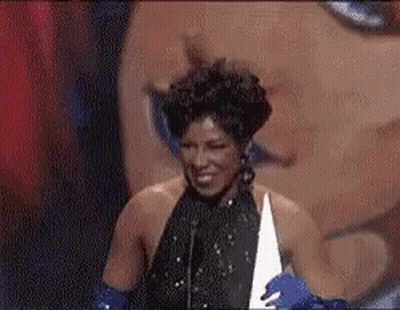 A Woman In A Black Dress And Blue Gloves Is Holding A Trophy And Smiling . GIF