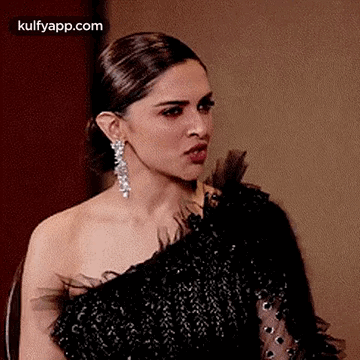 A Woman In A Black Dress And Earrings Is Making A Face . GIF