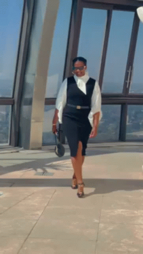 A Woman In A Black Dress And White Shirt Is Standing In Front Of A Window . GIF