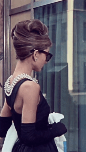 A Woman In A Black Dress Has A Pearl Necklace On Her Back GIF