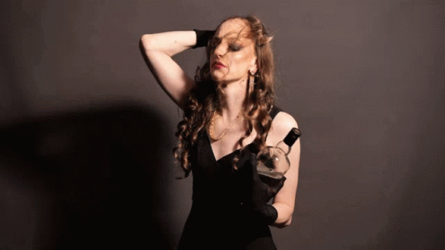 A Woman In A Black Dress Holding A Bottle Of Wine GIF