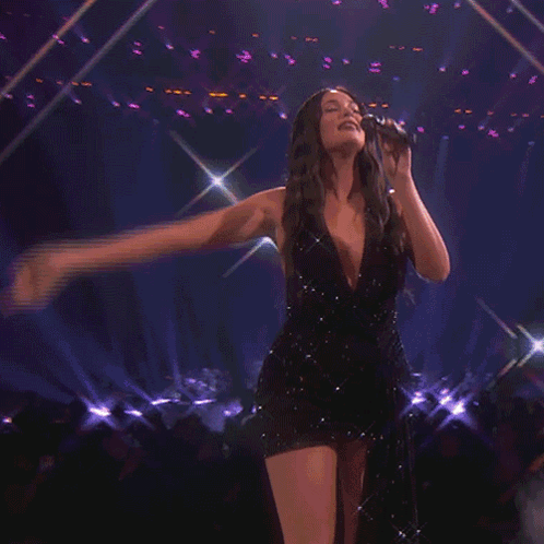 A Woman In A Black Dress Holds A Microphone In Her Hand GIF