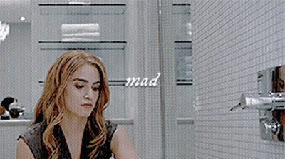 A Woman In A Black Dress Is Adjusting A Shower Head With The Word Mad Written On The Wall Behind Her GIF