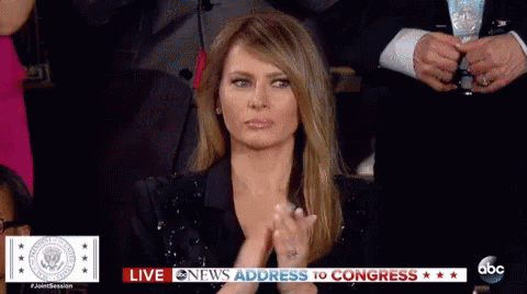 A Woman In A Black Dress Is Clapping Her Hands While Sitting In Front Of A News Screen . GIF