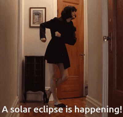 A Woman In A Black Dress Is Dancing In A Hallway With The Words A Solar Eclipse Is Happening Below Her GIF