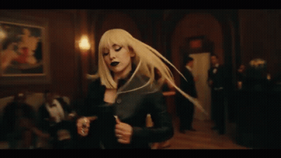 A Woman In A Black Dress Is Dancing In A Room Surrounded By Men In Suits . GIF