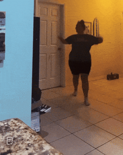 A Woman In A Black Dress Is Dancing In A Room With A Blue Wall GIF