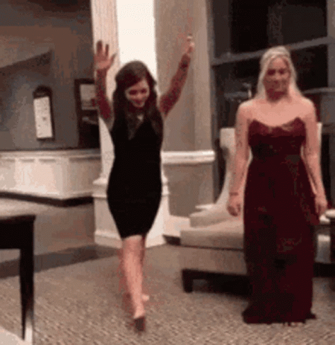 A Woman In A Black Dress Is Dancing In A Room With A Woman In A Red Dress . GIF