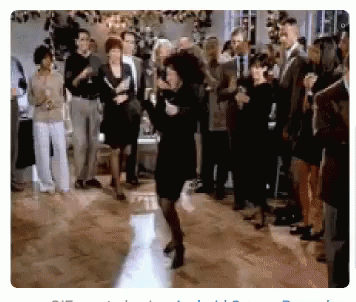A Woman In A Black Dress Is Dancing In Front Of A Crowd At A Party GIF