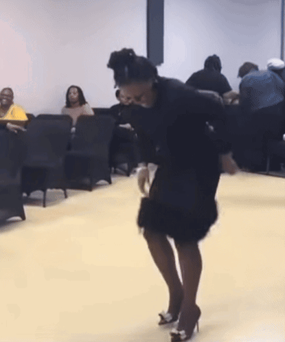 A Woman In A Black Dress Is Dancing In Front Of A Crowd Of People GIF