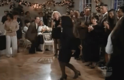 A Woman In A Black Dress Is Dancing In Front Of A Crowd Of People At A Party . GIF