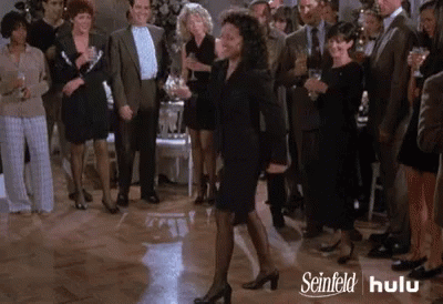 A Woman In A Black Dress Is Dancing In Front Of A Crowd Of People At A Party . GIF