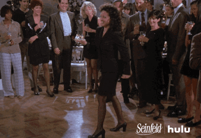 A Woman In A Black Dress Is Dancing In Front Of A Crowd Of People With The Words Seinfeld Hulu On The Bottom Right GIF
