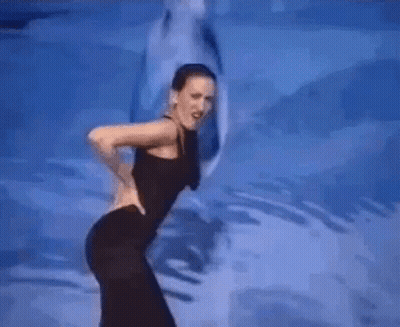 A Woman In A Black Dress Is Dancing In Front Of A Dolphin GIF