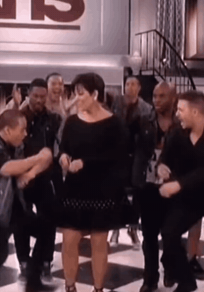 A Woman In A Black Dress Is Dancing In Front Of A Group Of People . GIF