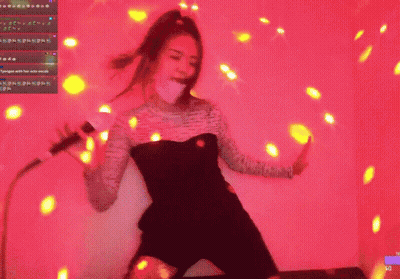 A Woman In A Black Dress Is Dancing In Front Of A Pink Background GIF