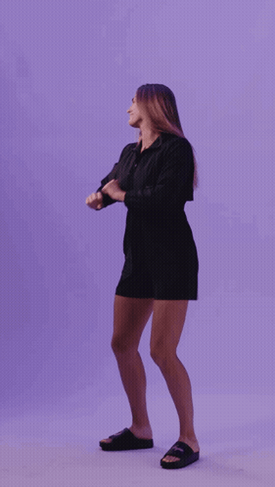 A Woman In A Black Dress Is Dancing In Front Of A Purple Wall GIF