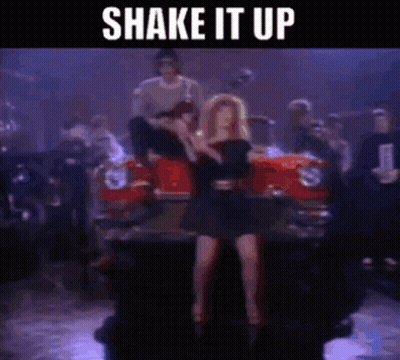 A Woman In A Black Dress Is Dancing In Front Of A Red Car With The Words Shake It Up Above Her GIF