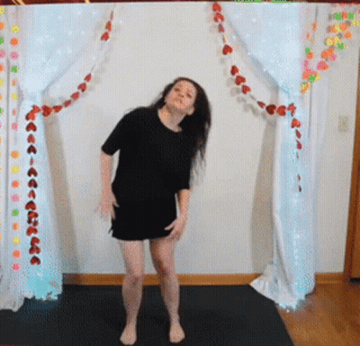 A Woman In A Black Dress Is Dancing In Front Of A White Curtain With Red Hearts On It GIF