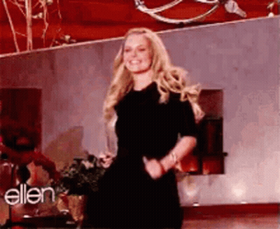 A Woman In A Black Dress Is Dancing On A Stage In Front Of A Wall With The Word Ellen On It . GIF