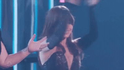 A Woman In A Black Dress Is Dancing On A Stage While A Man Holds Her Hand . GIF