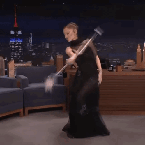A Woman In A Black Dress Is Dancing With A Mop In Her Hand GIF