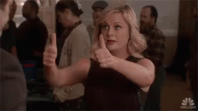 A Woman In A Black Dress Is Giving A Thumbs Up In A Crowded Room . GIF