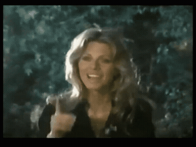 A Woman In A Black Dress Is Giving The Middle Finger While Standing In Front Of Trees . GIF