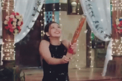A Woman In A Black Dress Is Holding A Bat In Her Hand And Throwing It In The Air . GIF